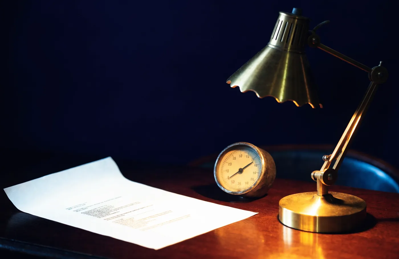 A round dial gauge and a report under a desk lamp