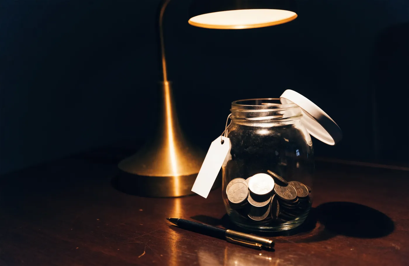 A jar of coins with a tag, partly open, under a desk lamp