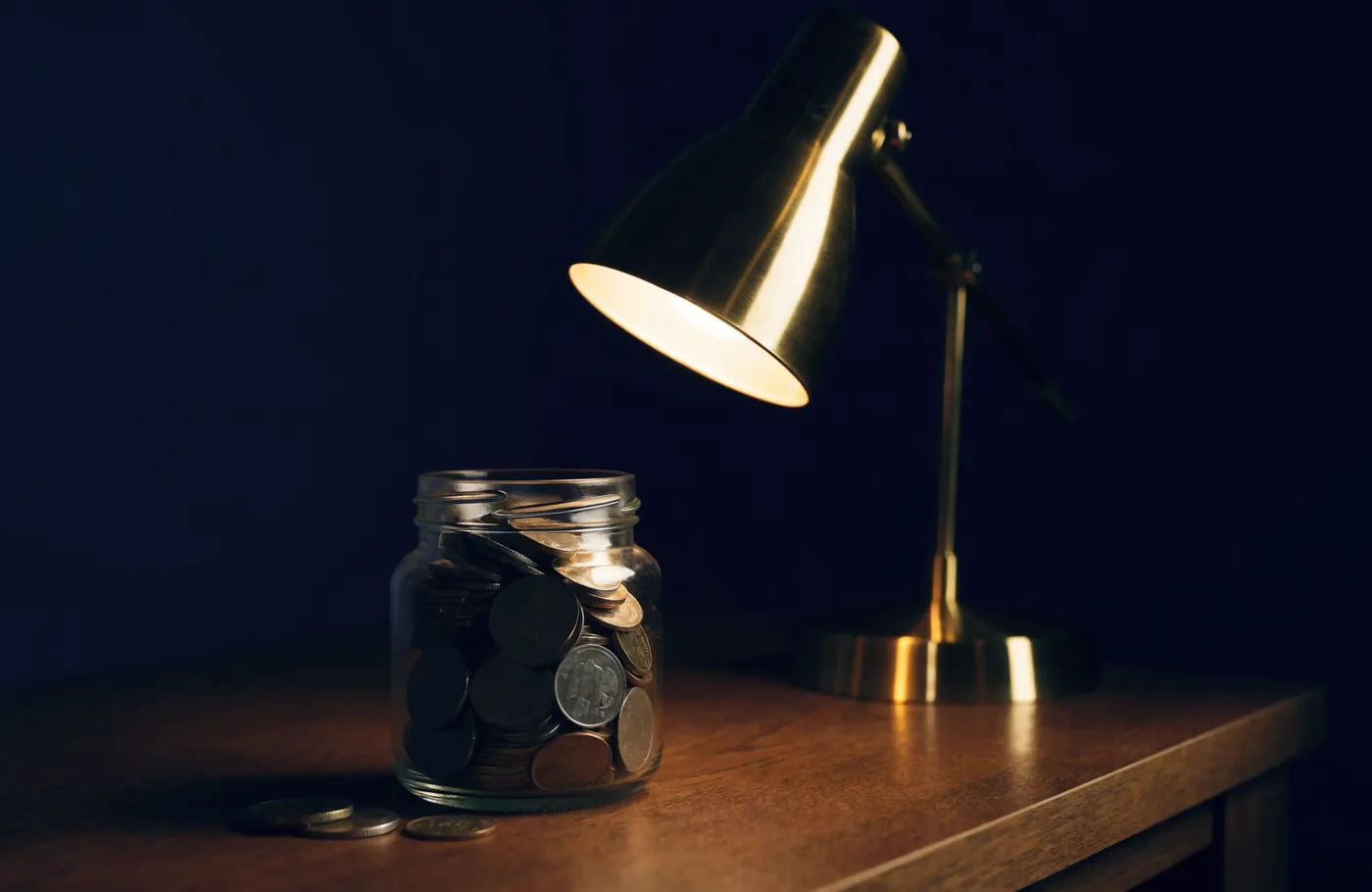 A jar of coins with a few taken out under a desk lamp