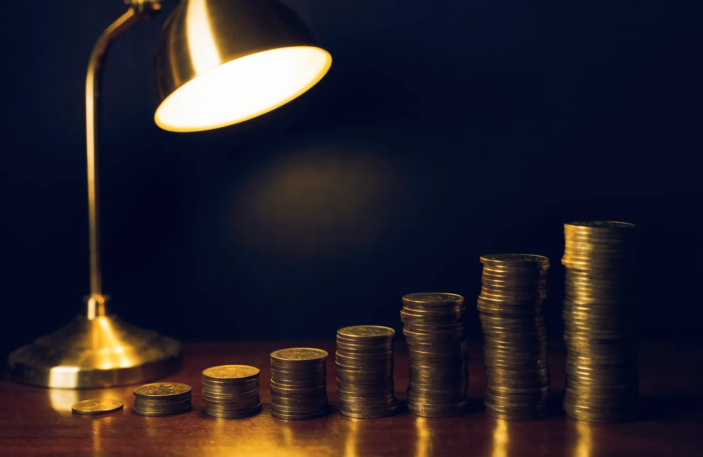 Coins stacked from small to large under a warm desk lamp