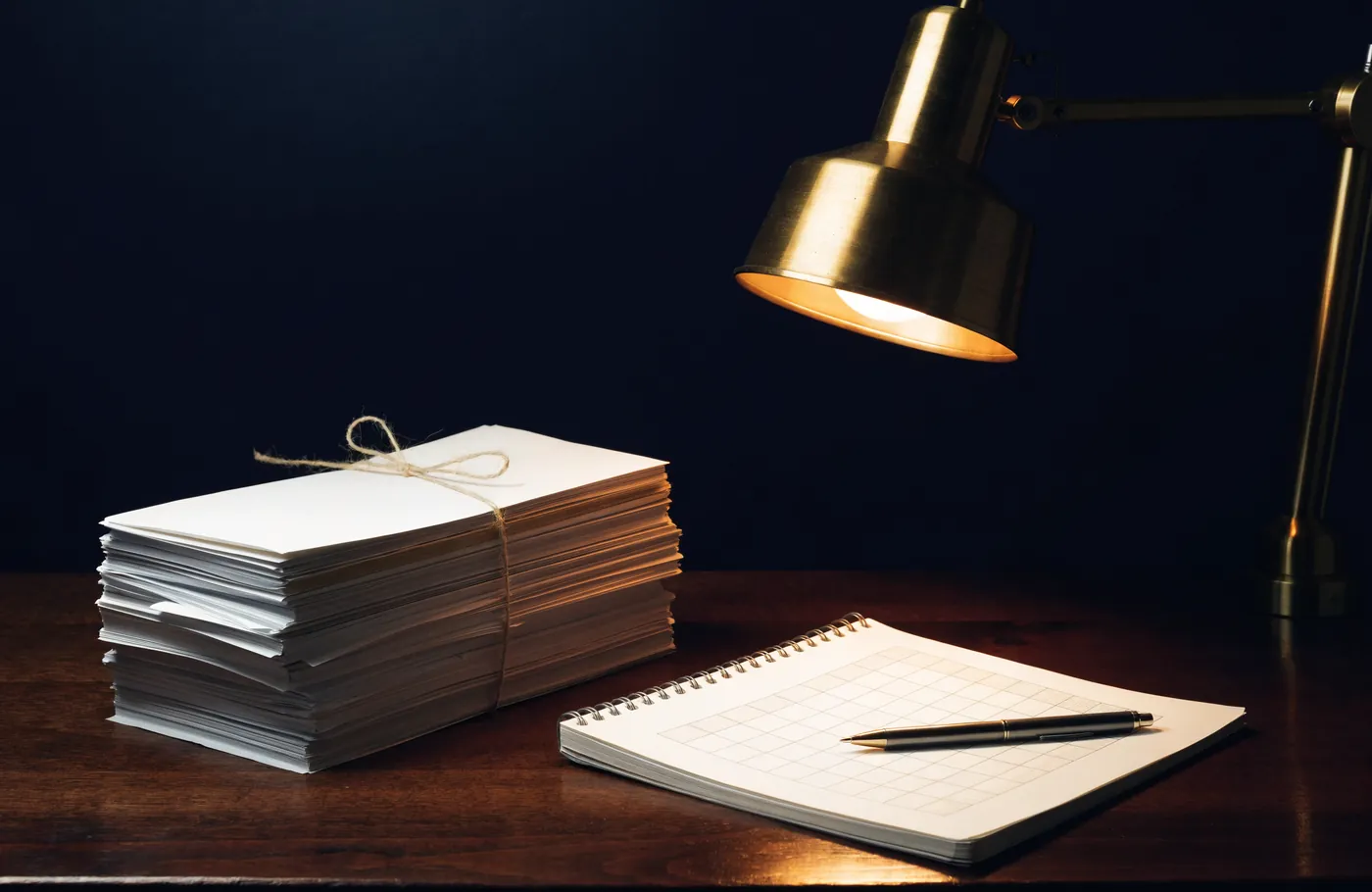 A neat stack of envelopes and a checklist under a desk lamp