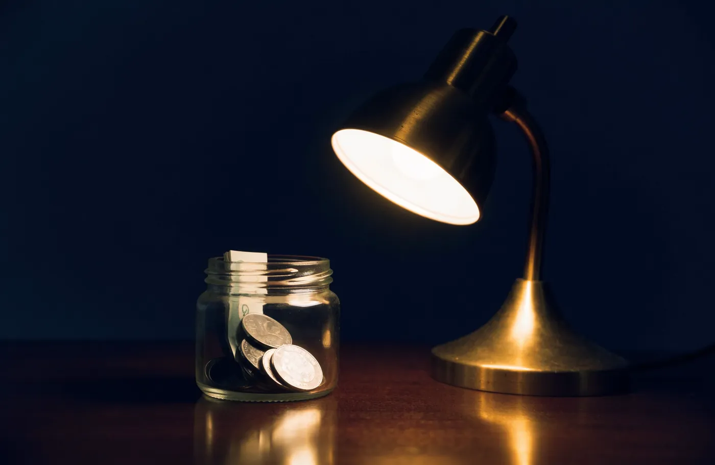 A glass jar of coins and a notebook under a warm desk lamp
